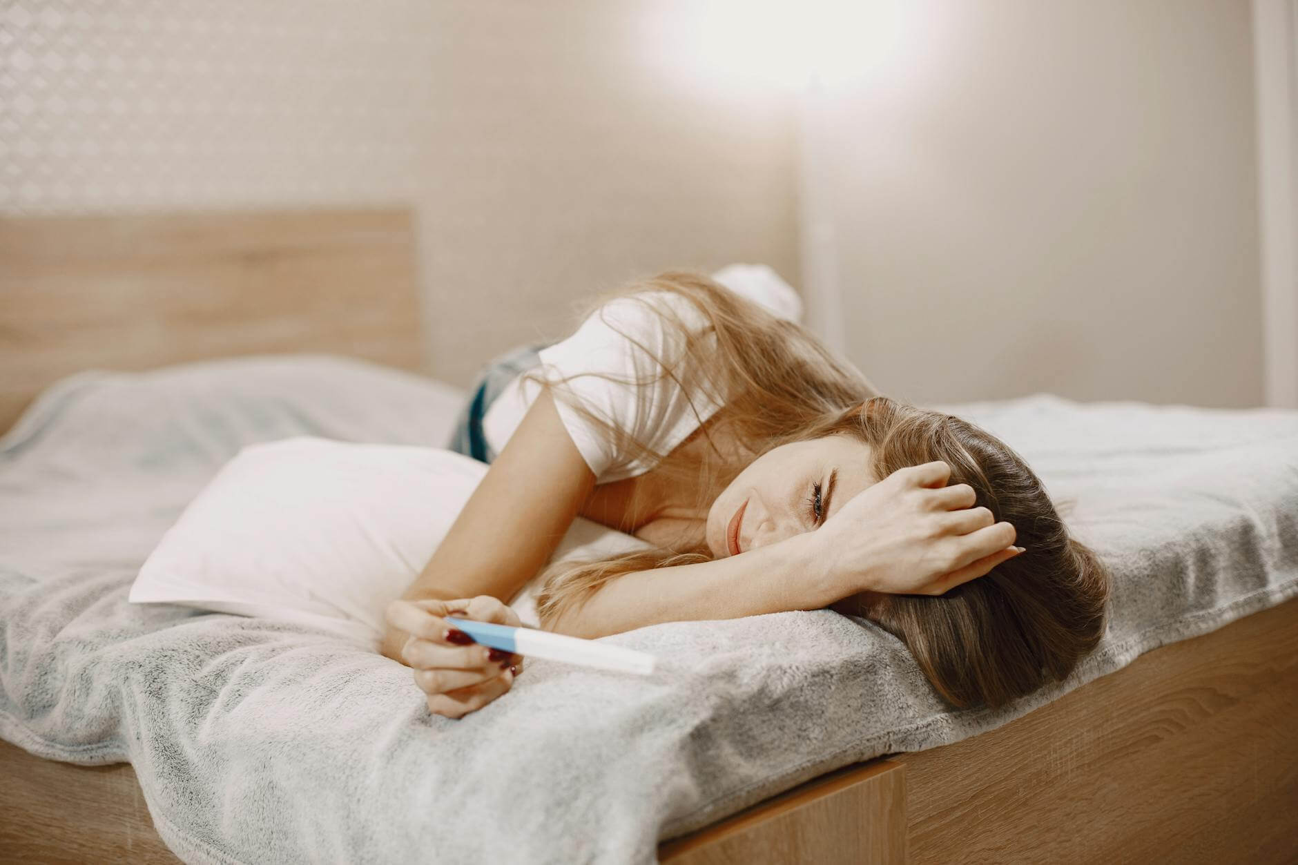 woman laying on the bed while holding a pregnancy test