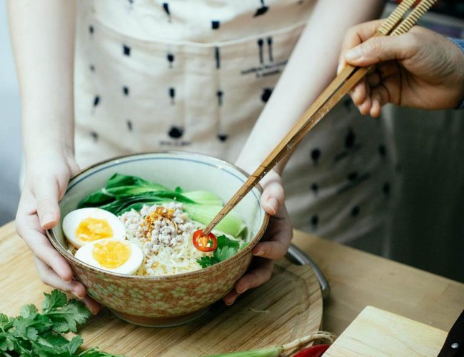 crop unrecognizable women garnishing asian soup with cut pepper