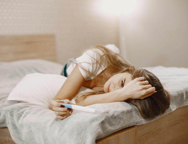 woman laying on the bed while holding a pregnancy test